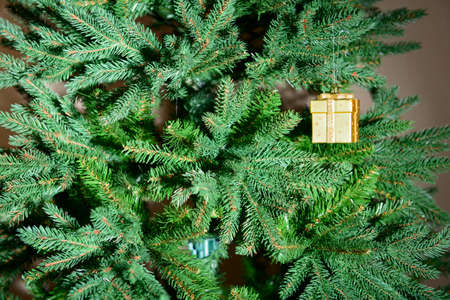 A Christmas tree toy in the form of a golden box hangs on the branches of the Christmas treeの写真素材