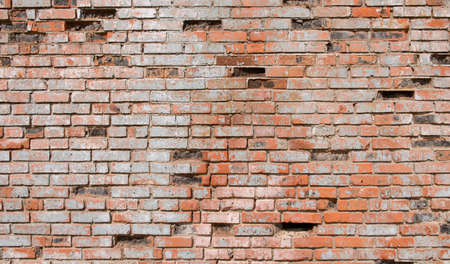 an old brick wall with cracks and fallen bricksの写真素材