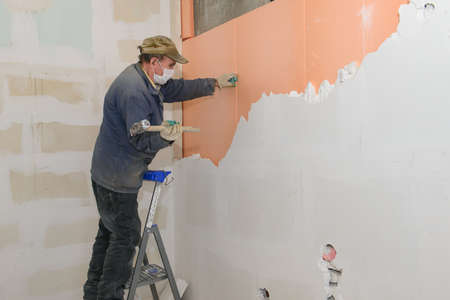 A worker on a stepladder breaks a wall of plaster blocksの写真素材