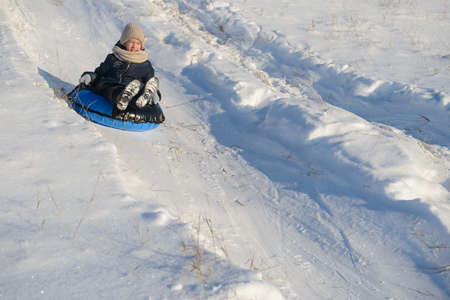 A happy girl rides a tubing from a snow slideの写真素材