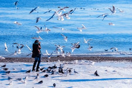 Girl covers her face from a flock of hungry gulls on a winter beachの写真素材