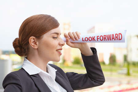 Businesswoman with papersheet twisted into a tube looks forward の写真素材