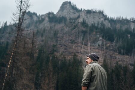 guy with a beard alone on a walk in the woods in a mountainous area. guy looks at the mountains....