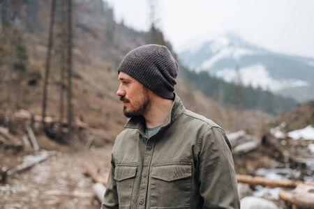 guy with a beard alone on a walk in the woods in a mountainous area. guy looks at the mountains. life in the woods outside the cityの写真素材