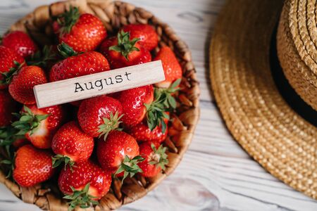 The inscription Augustus on the tree. Fresh juicy strawberries organic bio berries in a wicker basket on a rustic table.Eco, organic vegetarian summer diet food. Straw hat Sun glasses.の写真素材