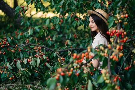 Portrait of a young cheerful woman in a straw hat with a basket cherries