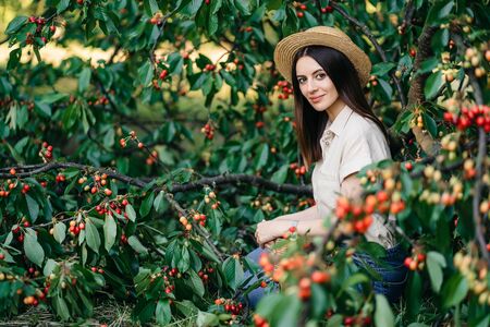 Portrait of a young cheerful woman in a straw hat with a basket cherriesの写真素材