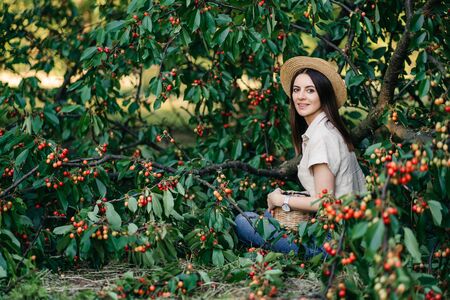 Portrait of a young cheerful woman in a straw hat with a basket cherries