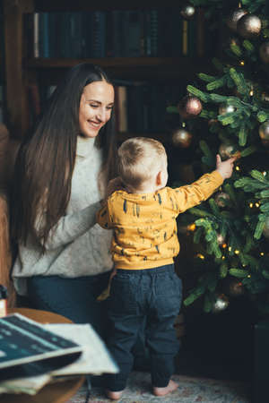 happy mom with her little son decorate the Christmas tree, hang balls on the Christmas treeの写真素材