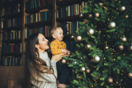 happy mom with her little son decorate the Christmas tree, hang balls on the Christmas tree