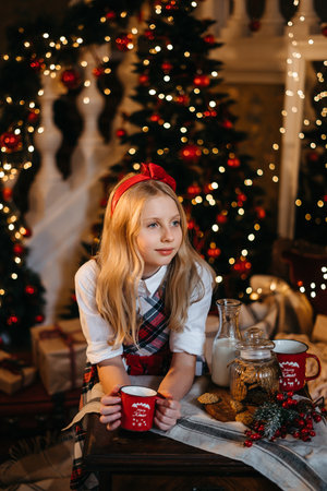 Good New Year spirit. Little blonde girl sitting near a Christmas tree with a gift waiting for Santa. High quality photoの写真素材
