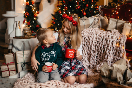 Little boy and girl are sitting near the Christmas tree and hugging. Happy brother and sister. High quality photoの写真素材