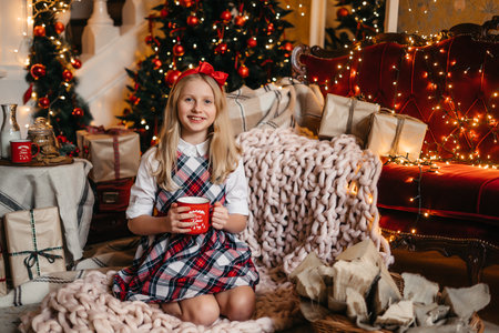 Good New Year spirit. Little blonde girl sitting near a Christmas tree with a gift waiting for Santa. High quality photoの写真素材