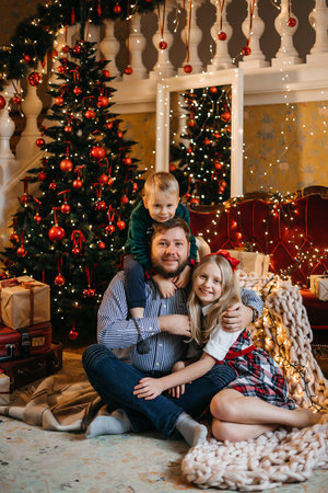 Close up overjoyed family unpacking Christmas gifts, happy father with adorable little daughter and son wearing sweaters sitting on warm floor near decorated festive tree at home. High quality photoの写真素材