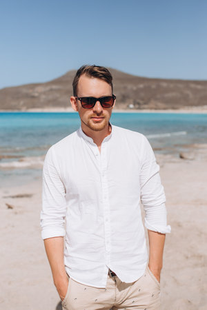 portrait of a young man in sunglasses and a white shirt against the background of the sea and rocks. Sumer holidays . High quality photoの写真素材