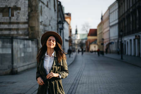 Outdoor fashion portrait of elegant, luxury woman wearing beige hat, sunglasses, trendy white shirt, in a green trench coat, walking in street. Copy, empty space for text. High quality photoの写真素材