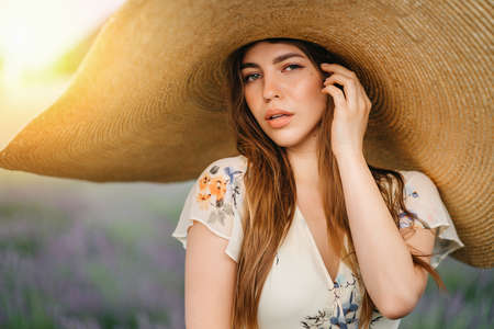 Beautiful young woman portrait in lavender field. An attractive girl with long curly hair in a long dress is dreaming. High quality photoの写真素材