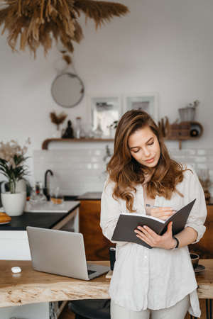 portrait of young woman in comfortable clothes with notepad, planning work and expenses at home. High quality photoの写真素材