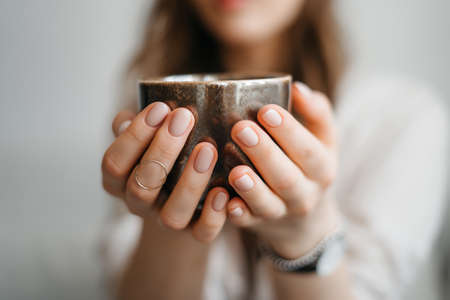 Female hands hands holding cup of tea. Tea time. Cosy photo with blurred background. Natural light, selective focus. Close up. High quality photoの写真素材