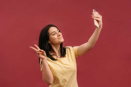 Image of joyful caucasian woman holding cellphone and gesturing ok sign while winking isolated over...