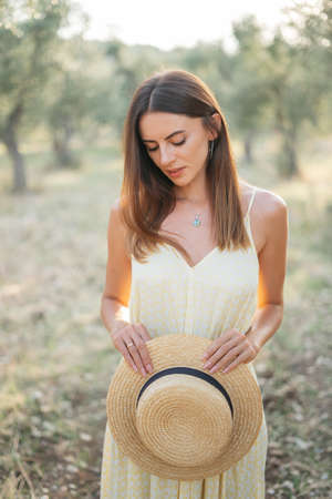 Tender portrait of beautiful brunette woman in beautiful sunlight. Woman in yellow summer linen dress in olive tree garden. Natural beauty.Travel to Italy, summer vacation. High quality photoの写真素材