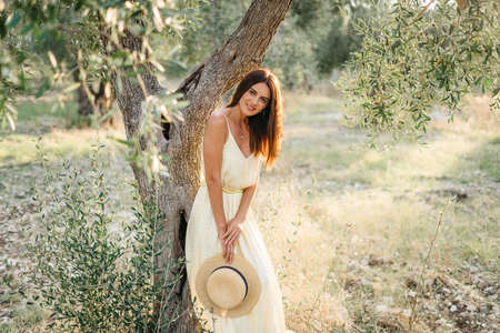 Tender portrait of beautiful brunette woman in beautiful sunlight. Woman in yellow summer linen dress in olive tree garden. Natural beauty.Travel to Italy, summer vacation. High quality photoの写真素材