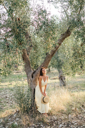 Tender portrait of beautiful brunette woman in beautiful sunlight. Woman in yellow summer linen dress in olive tree garden. Natural beauty.Travel to Italy, summer vacation. High quality photoの写真素材