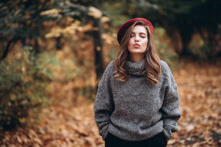 Portrait of a joyful young woman enjoying in the autumn park. beautiful blonde girl in autumn red beret and gray sweater. Relax in nature. High quality photoの写真素材