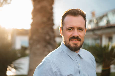 Portrait of happy mature man looking at camera outdoor. Senior businessman with beard feeling confident at sunset. Closeup face of business man smiling with city in background. High quality photoの写真素材
