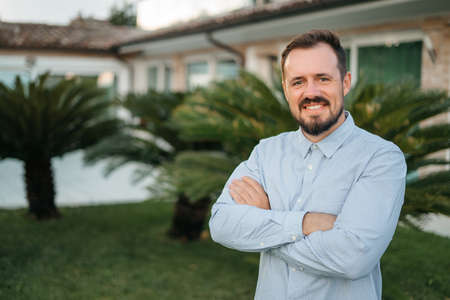 portrait of a young handsome man smiling outdoor. Man near his new home in the garden. High quality photoの写真素材