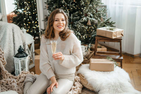 Happy young woman stretches out her hand with a glass of sparkling wine, looks at the camera, celebrates New Years Christmas holidays, congratulates the family with a video call. High quality photoの写真素材
