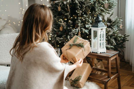 Focus on wrapped Christmas present congratulating with winter holidays, reminding preparing gifts, posing near decorated tree. High quality photoの写真素材