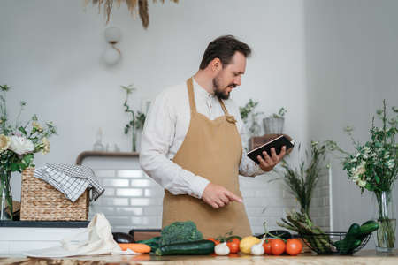 Handsome man with green ingredients and spicy herbs preparing healthy food in the kitchen. High...