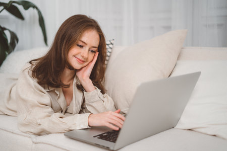 Young pretty redhad woman student using laptop elearning or remote working at home office looking at laptop computer watching webinar, learning virtual class, having video call hybrid meetingの写真素材