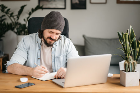 Man taking notes down from his new laptop computer at work in the morning office with coffee. High quality photoの写真素材