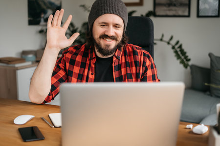Friendly confident young adult caucasian broker, freelancer or manager in formal clothes and glasses using laptop, talk to colleagues or clients on conference call, greeting hand gesture, smilingの写真素材
