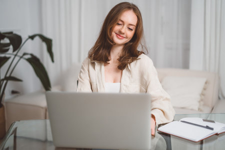 Successful positive young adult woman freelancer, manager, CEO, sitting in office at laptop, talking on video call with client or employees, discussing business strategy, gesturing,smile.の写真素材