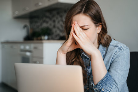 Female freelance with eyes closed is massaging head temples with suffering face expression. Tired and worn out from online work young woman sitting in front laptop holding head. High quality photoの写真素材