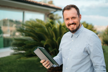 Portrait of a young handsome man with a beard smiling outdoors uses a tablet. Modern technologists outside the city. High quality photoの写真素材
