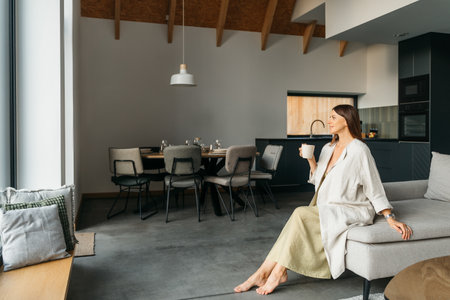 Woman sitting on couch in living room at home, enjoying coffee. High quality photoの写真素材