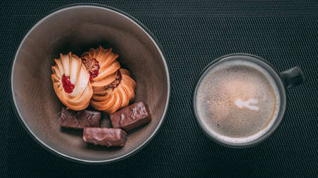 stylish photo of coffee with foam in a black mug top view with sweets and cookies, on a dark background, natural lighting.の写真素材
