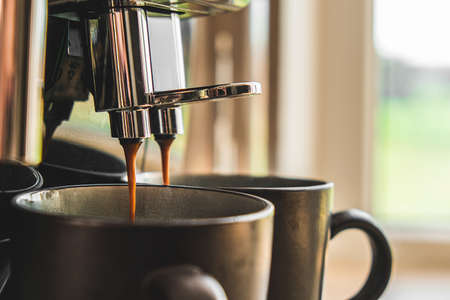 The coffee machine makes coffee in two mugs. coffee flows from the tubes. close-up. selective focusの写真素材