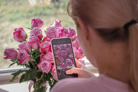 girl photographs a bouquet of flowers on a smartphone. flowers in the background, focus on the smartphone screen. selective focusの写真素材
