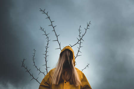 a girl with long hair in a yellow hood, with the back of a tree with thorns. the concept of depression, mysticism, dark thoughtsの写真素材
