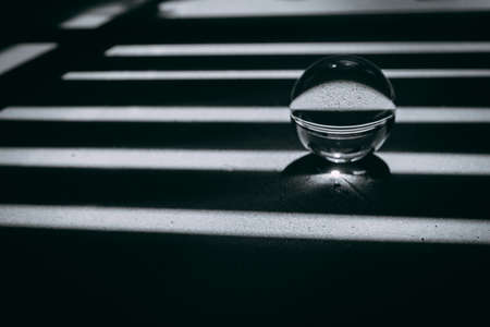 glass transparent ball rolls along dark and light lines, light and shadow. the concept of good luck and bad luck in life.の写真素材
