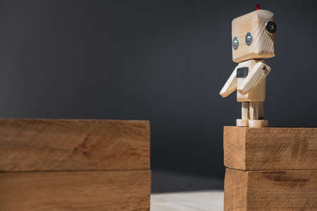 a small wooden robot stands on the edge of a cliff made of wooden blocks.の写真素材