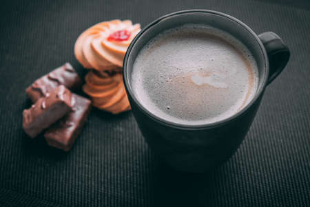 stylish photo of coffee with foam in a black mug top view with sweets and cookies, on a dark background, natural lighting.の写真素材
