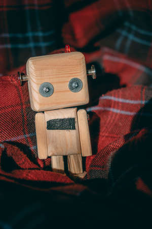 diy wooden toy robot stands wrapped in a cozy checkered red blanket. loneliness conceptの写真素材