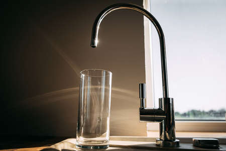empty glass and tap with clean water in the morning sun. a glass of water in the morning. healthy eating, health careの写真素材