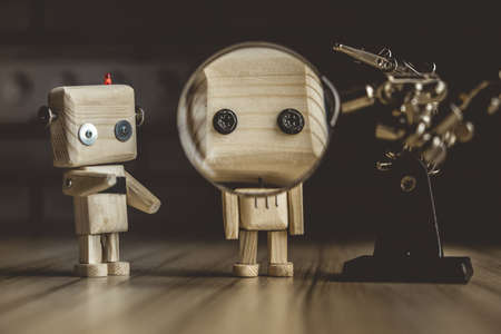 wooden robot android stands on a table under a magnifying glass. metal clamps with a magnifying...